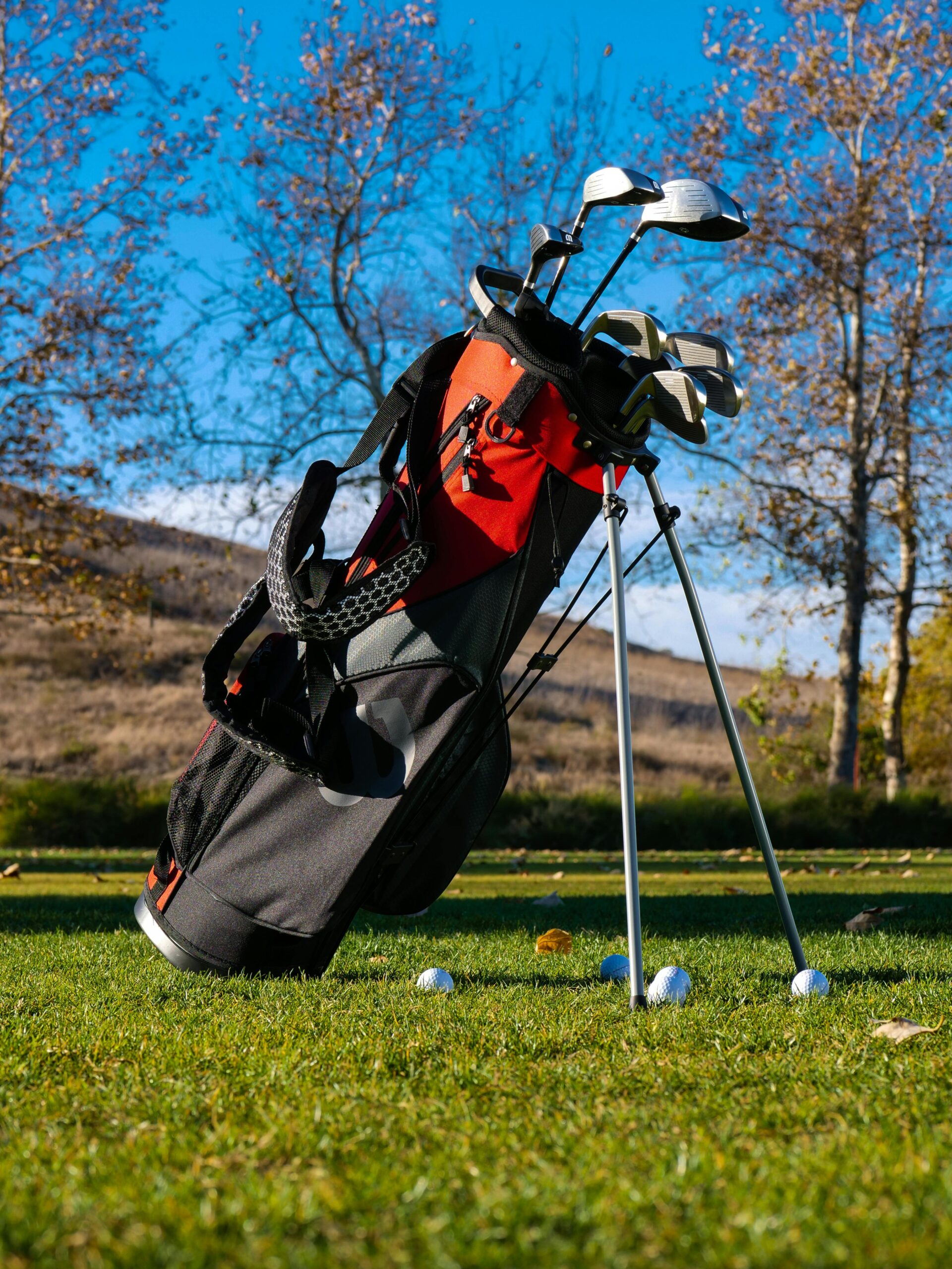 A well-organized golf bag with clubs on a grassy golf course under clear blue skies.